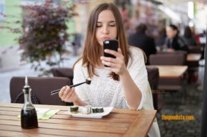 Mindfulness is about appreciating the moment, which social media can destroy in this post on thegoodista.com. Illustrated by young woman eating while looking at her phone.